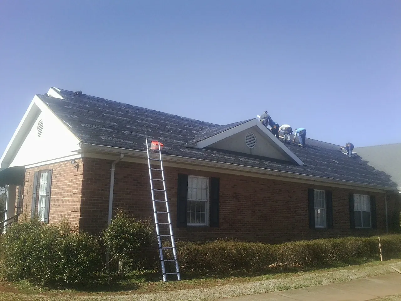 Crew tearing shingles off a brick ranch roof with a ladder set in Saint Marys