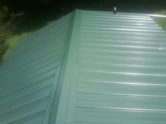 New green metal panels meeting at the ridge of a roof — Flat Roof Repair work by our crew in Saint Marys